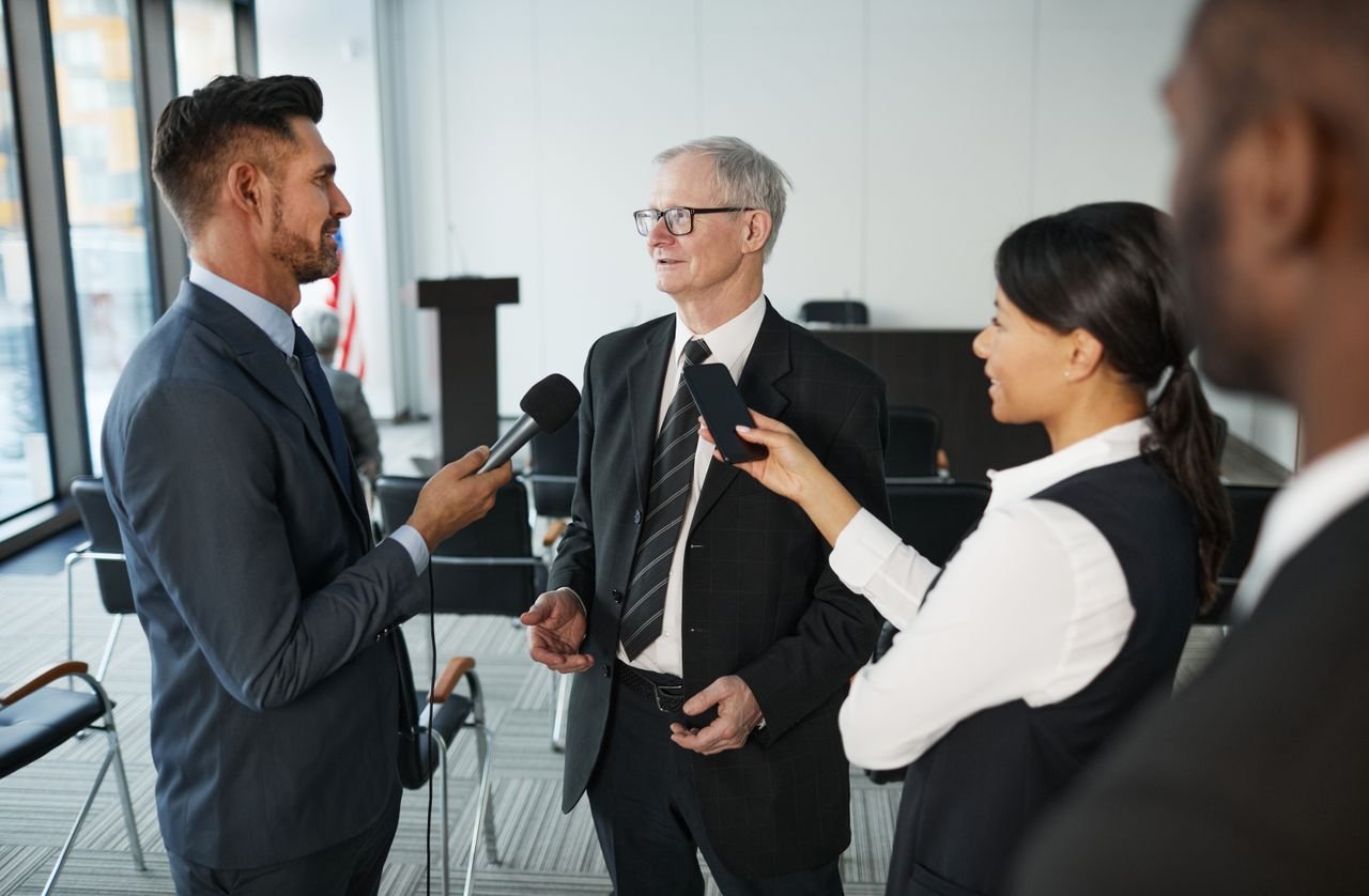 about-us Journalists conduct an interview with a senior executive in a formal office setting.